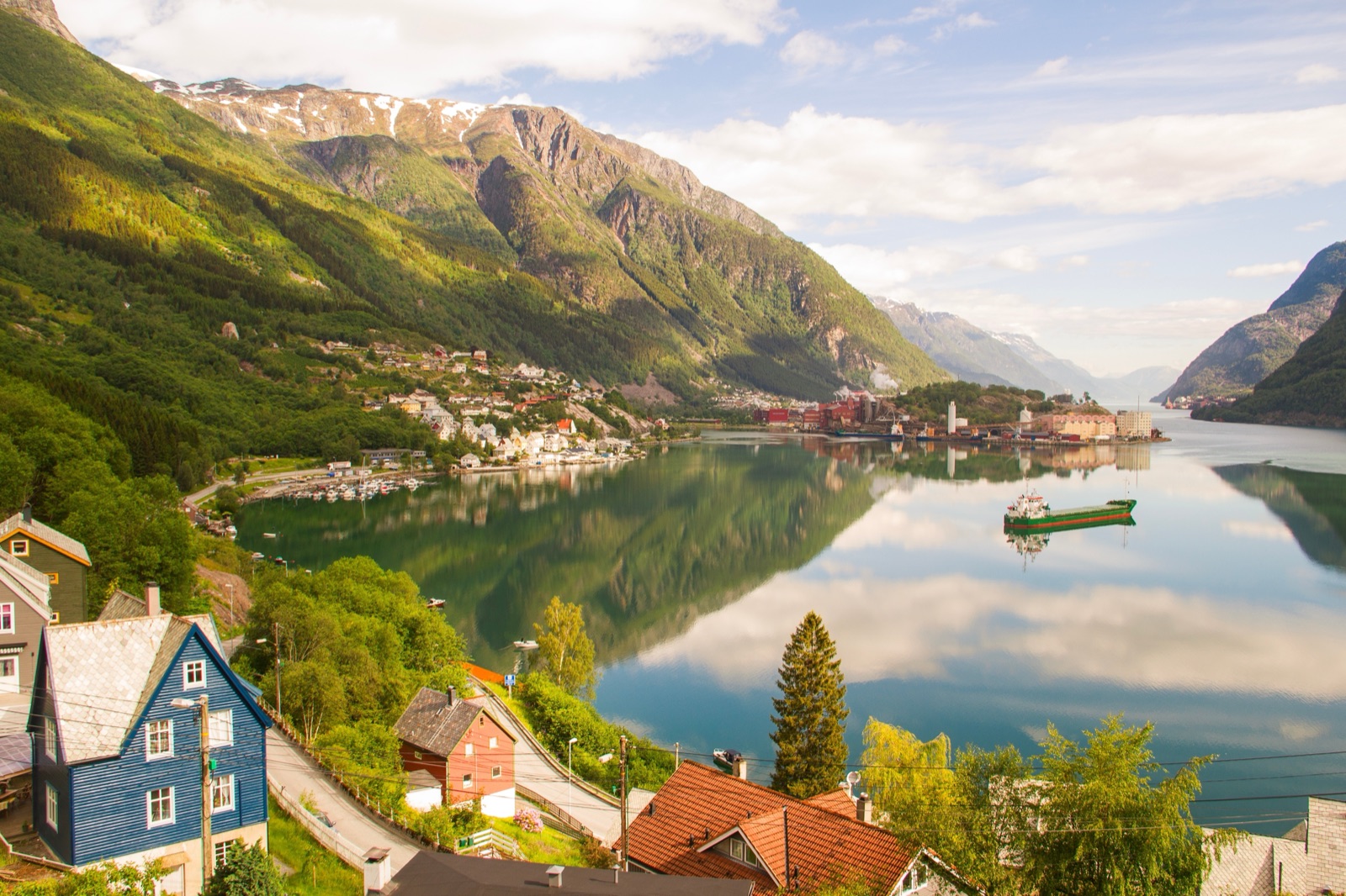 Hus og en kai ved fjorden i Odda, speilet i stille vann under grønne fjell